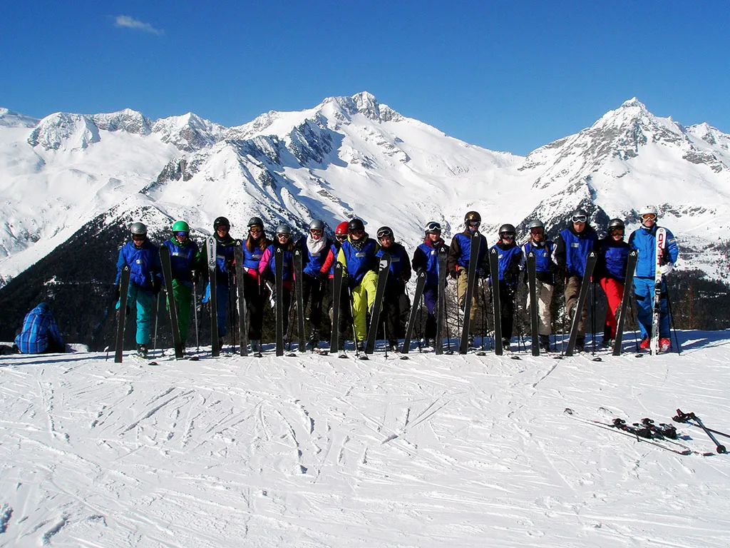 Große Skigruppe steht in einer Reihe vor dem Bergpanorama.